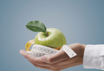 Nutritionist holding a tape measure and an apple, fitness and diet plan concept