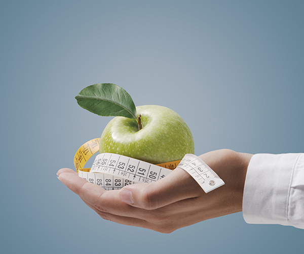 Nutritionist holding a tape measure and an apple, fitness and diet plan concept