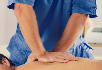 Physiotherapist doing healing treatment on man's back. Therapist wearing blue uniform. Osteopathy. Chiropractic adjustment, patient lying on massage table