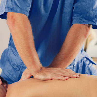 Physiotherapist doing healing treatment on man's back. Therapist wearing blue uniform. Osteopathy. Chiropractic adjustment, patient lying on massage table